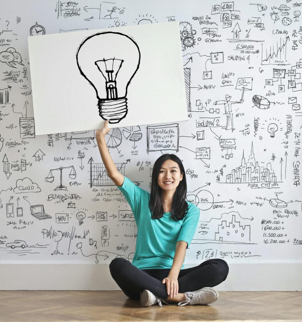 Une jeune femme tient un dessin d'ampoule contre un mur de brainstorming créatif.