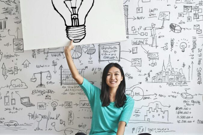 Une jeune femme tient un dessin d'ampoule contre un mur de brainstorming créatif.
