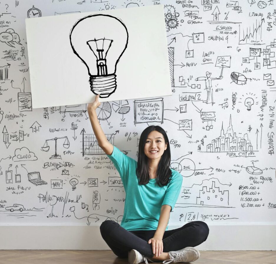 Une jeune femme tient un dessin d'ampoule contre un mur de brainstorming créatif.