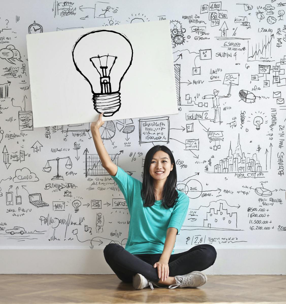 Une jeune femme tient un dessin d'ampoule contre un mur de brainstorming créatif.