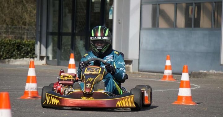 Pilote de kart bleu navigant entre des cônes sur une piste devant un bâtiment