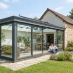 Véranda moderne en aluminium accolée à une maison, baies vitrées, jardin ensoleillé