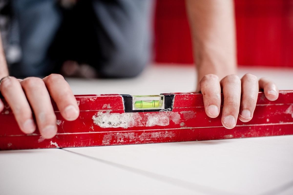 Mains d'un ouvrier positionnant un niveau rouge sur une surface de travail blanche Mains d'un ouvrier positionnant un niveau rouge sur une surface de travail blanche