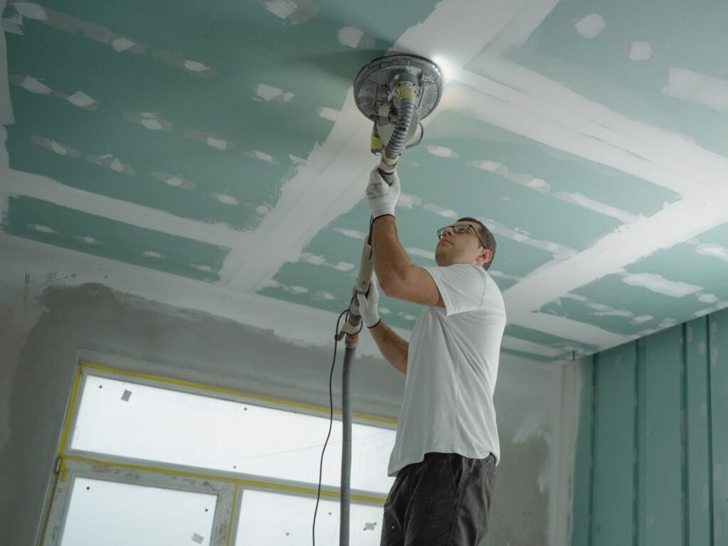 Un ouvrier utilise une ponceuse sur le plafond d'une pièce en travaux