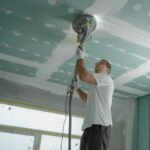 Un ouvrier utilise une ponceuse sur le plafond d'une pièce en travaux