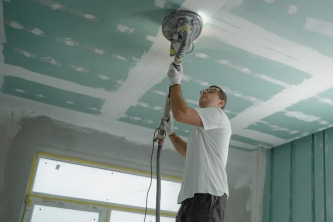 Un ouvrier utilise une ponceuse sur le plafond d'une pièce en travaux