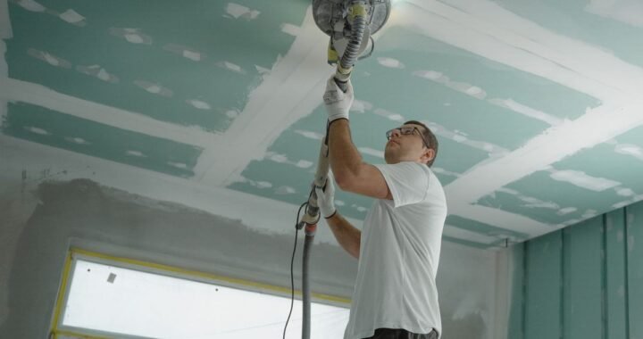 Un ouvrier utilise une ponceuse sur le plafond d'une pièce en travaux
